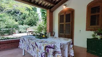 Un portico coperto con un tavolo apparecchiato per mangiare, circondato da muri in mattoni e persiane di legno.