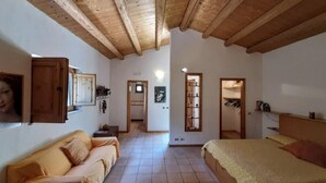 A room with a wooden ceiling, a sofa, a bed, a wardrobe, and a hallway leading to another room. - Villa de Leva - Casa Gialla (Modica)