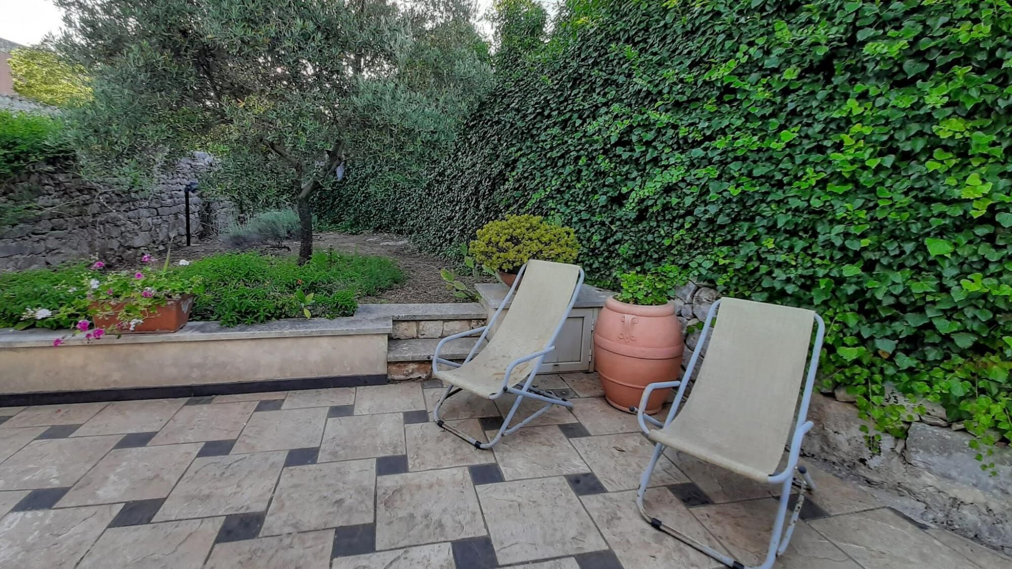 A patio with two metal chairs, a stone wall, and a variety of plants.