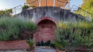 A stone bridge with a brick archway, surrounded by lush greenery and potted plants. - Villa de Leva - Casa Verde (Modica)