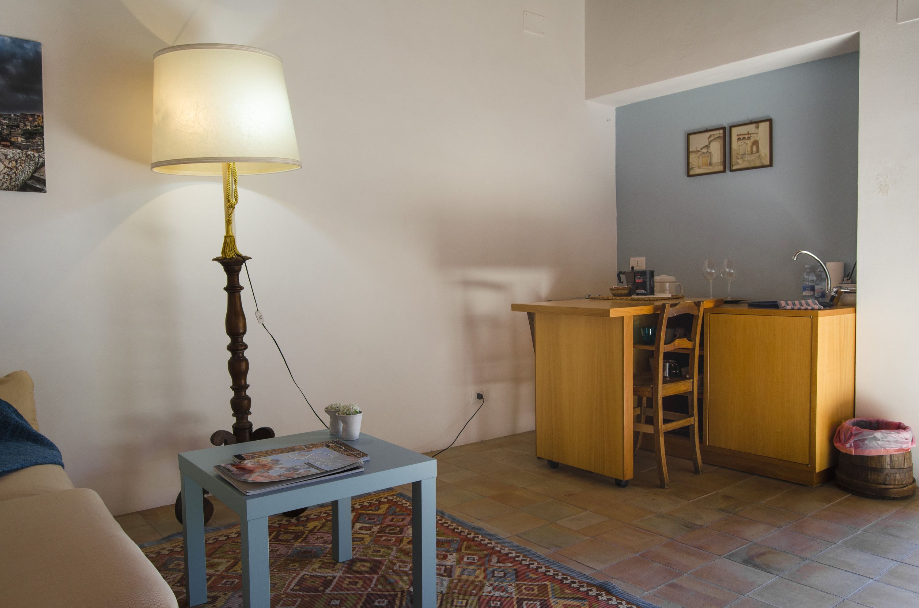 A small living area with a sofa, a table with a lamp, a kitchen area with a sink, and a chair.
