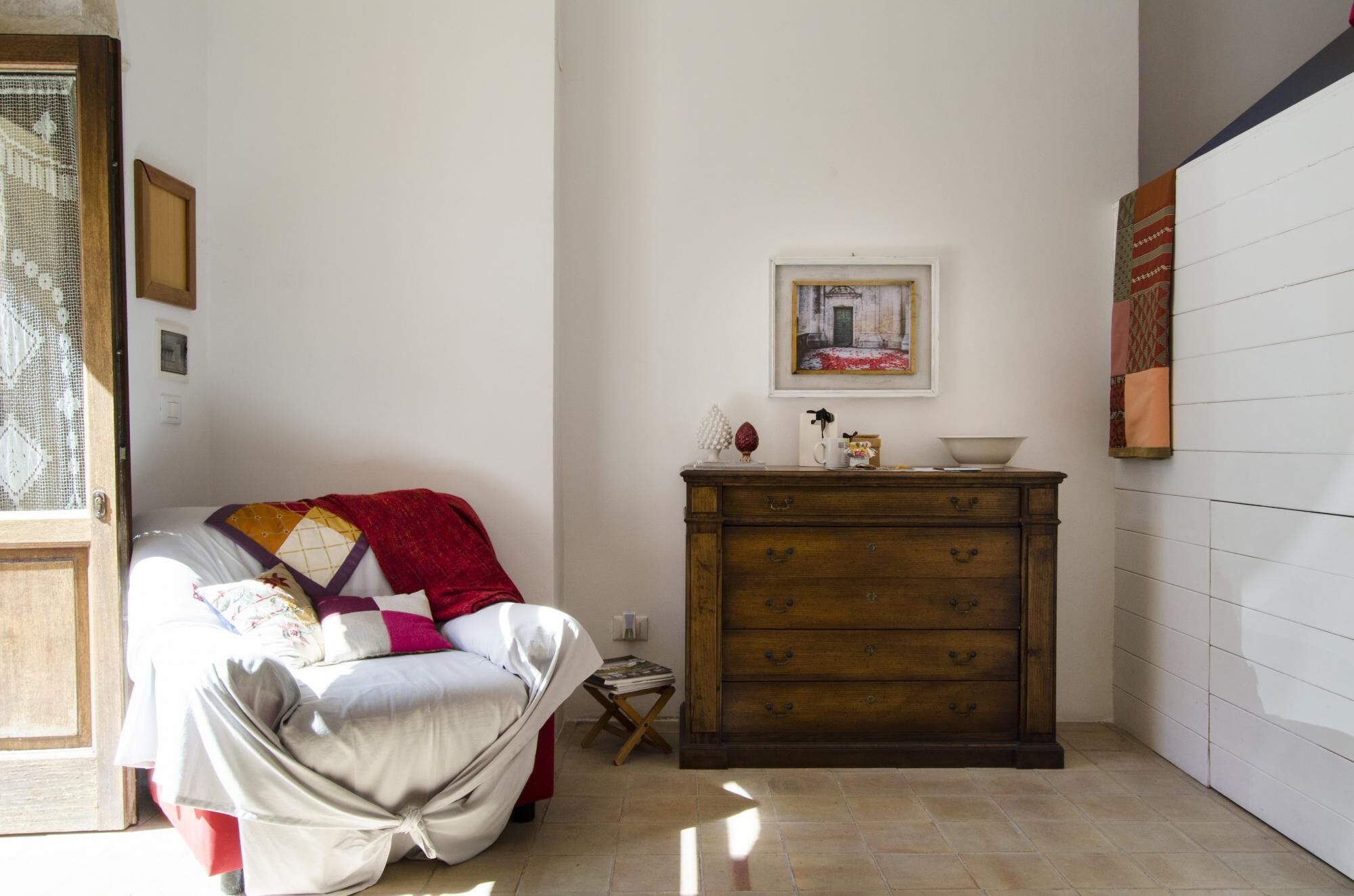 Habitació acollidora amb un llit cobert per un llençol de colors, una petita estanteria de fusta amb calaixos, un quadre encapçalat a la paret i una porta amb una cortina de galeria.
