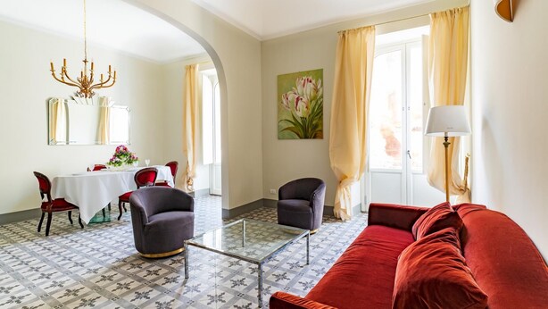 A living room with a red sofa, a glass coffee table, and a dining area with a white table and red chairs. - Capo 10 Liberty C3 in Siracusa (Syracuse)