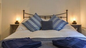 A neatly made bed with striped pillows, a grey blanket, and folded towels on a metal bed frame. - 3 bedroom accommodation in Whatstandwell, near Matlock (Whatstandwell, near Matlock)