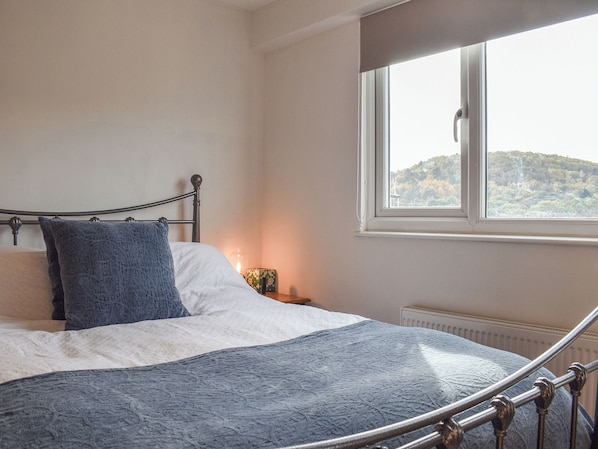 Ein Bett mit Kopfteil, ein Nachttisch mit Lampe und ein Fenster mit Blick auf eine Hügel.