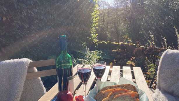 A picnic setup with a bottle, glasses, cheese, grapes, and bread on a wooden table. - 3 bedroom accommodation in Whatstandwell, near Matlock (Whatstandwell, near Matlock)