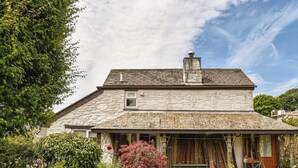 A stone house with a sloped roof, a chimney, and a porch with a bench. - 1 bedroom accommodation in Crows Nest, near Liskeard (Crows Nest, near Liskeard)