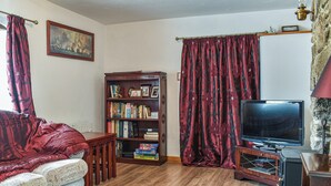 A living room with a wooden floor, a red sofa, a bookshelf, a flat-screen TV, and red curtains. - 1 bedroom accommodation in Crows Nest, near Liskeard (Crows Nest, near Liskeard)
