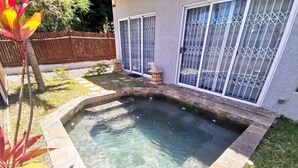 A rectangular swimming pool with a stone border, surrounded by a grassy yard and a wooden fence.