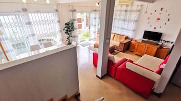 Un salon moderne avec un canapé rouge, un téléviseur et un escalier menant à une autre pièce.