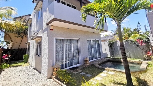A two-story house with a covered patio, a small pool, and a garden with palm trees.