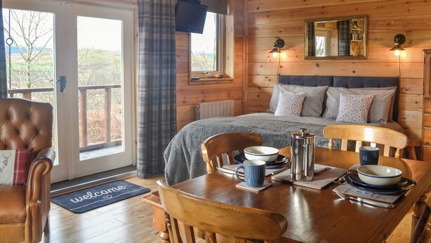 A cozy cabin interior with a bed, a dining table set with a coffee pot, bowls, and a mug.