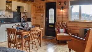 A wooden interior with a dining area, kitchen, and a cozy seating area with a leather armchair and a cushioned chair.
