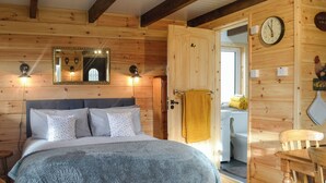A wooden cabin bedroom with a bed, a mirror, a clock, and a door leading to a bathroom.
