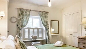 A neatly arranged bedroom with a bed, a bedside table, a mirror, and a window with curtains.