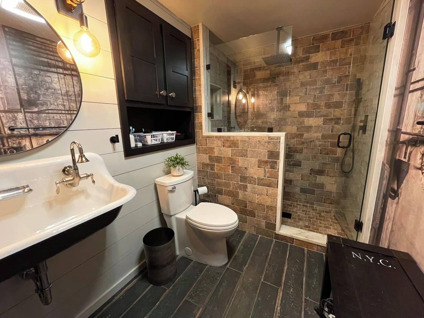 Ein Badezimmer mit einem weißen Waschbecken, schwarzen Schränken, einer Toilette und einem Duschbereich mit Backsteinwand.