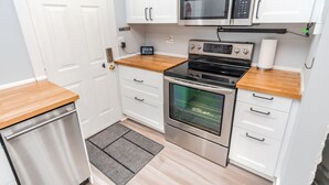 Une cuisine de taille réduite avec des meubles blancs, des appareils en acier inoxydable et un plan de travail en bois.