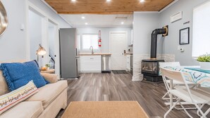 Un salon moderne avec un canapé, une table basse et un coin repas comprenant une table et des chaises. Au fond, on aperçoit une cuisine équipée d’un réfrigérateur, d’un évier et d’une cuisinière.