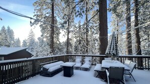 En snedækket terrasse med udendørs møbler, omgivet af høje, eviggrønne træer.