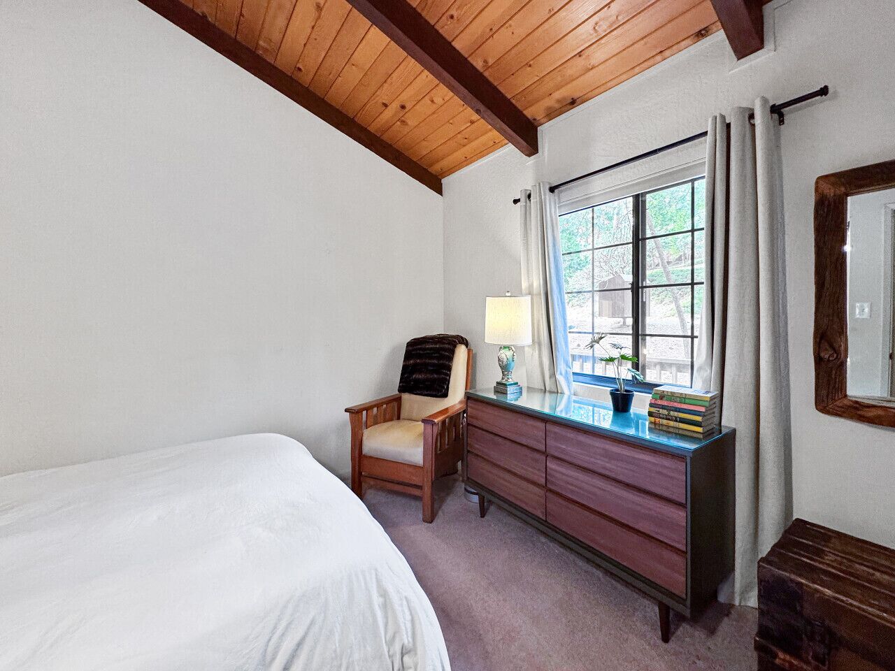 A bedroom with a bed, a chair, a dresser, a lamp, and a window with curtains.