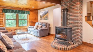 A log cabin interior with a fireplace, wooden walls, a sofa, and a window.