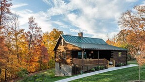 A log cabin with a metal roof, a porch, and a stone foundation.