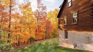 A log cabin with a grassy yard and autumn foliage.