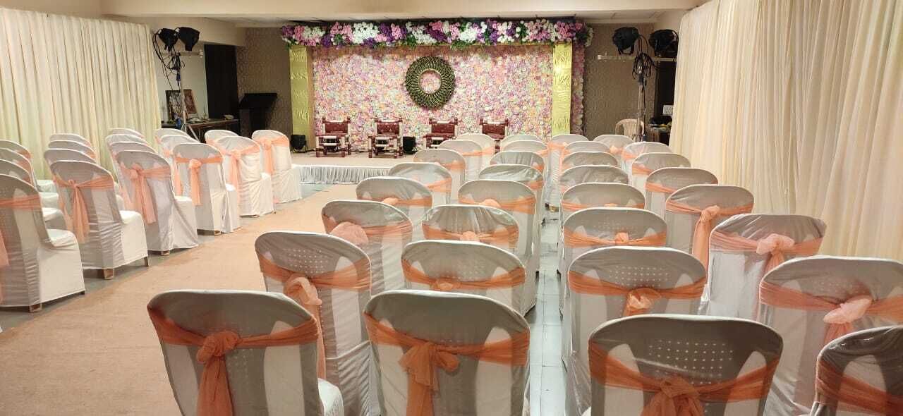 A banquet hall with rows of chairs tied with orange sashes, a stage with a floral backdrop, and a circular wreath above the stage.