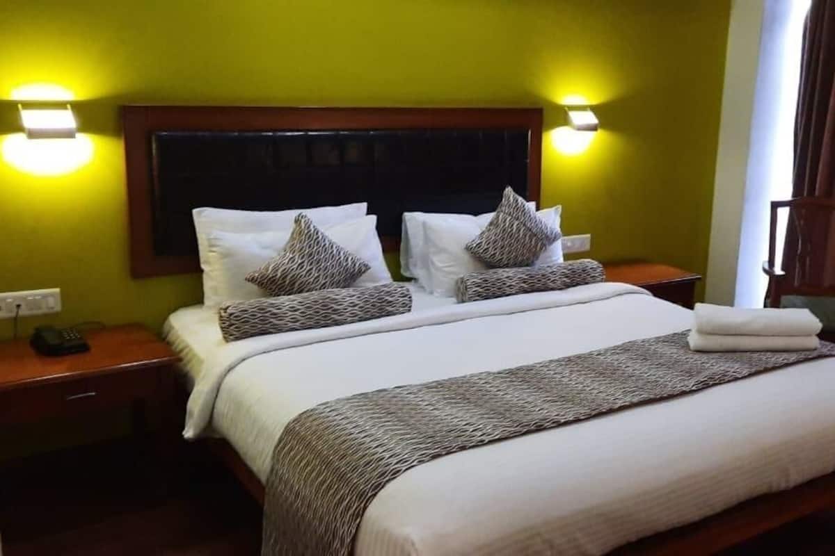 Habitación de hotel con una cama grande, dos mesitas de noche, una mesita auxiliar, cabecera de madera y dos lámparas de pared.
