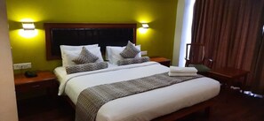 Une chambre d’hôtel avec un grand lit, deux tables de chevet, une petite table d’appoint, une tête de lit en bois et deux lampes fixées au mur.