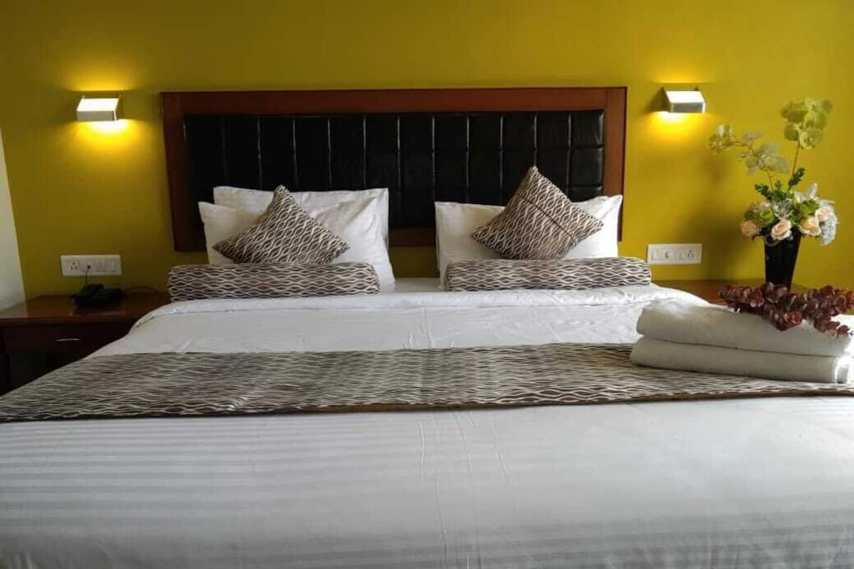 Una habitación de hotel con una cama grande, dos mesitas de noche, una lámpara de pared y un jarrón con flores.