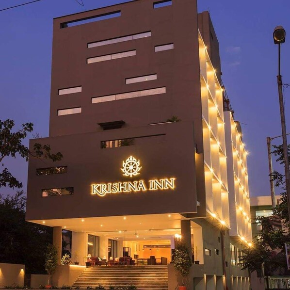 Un bâtiment moderne avec une enseigne indiquant « KRISHNA INN » et une entrée bien éclairée, accessible par quelques marches.