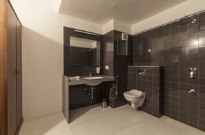 Une salle de bain moderne avec un mur recouvert de carreaux foncés, un lavabo blanc, des toilettes et un espace douche.