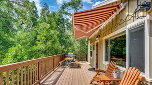 Une terrasse en bois avec une table de pique-nique et des chaises, un barbecue et un grand auvent à rayures.