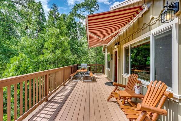 Une terrasse en bois avec une table de pique-nique et des chaises, un barbecue et un grand auvent à rayures.