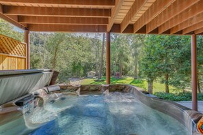 Un espace avec un jacuzzi, surmonté d’une pergola en bois et entouré d’une végétation luxuriante.