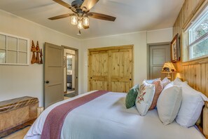 Une chambre à coucher avec un lit, une tête de lit en bois, un ventilateur de plafond et une fenêtre donnant sur un beau paysage.
