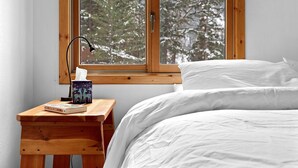 A bedroom with a wooden nightstand, a bedside table, a lamp, a book, and a window with a view of trees. - Fish, float, or raft out of your front door, MT's wilderness at your fingertips! (Bonner)