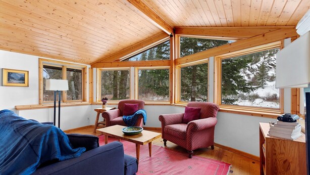 A cozy room with a wooden ceiling, large windows, a sofa, two armchairs, a small table, and a bookshelf. - Fish, float, or raft out of your front door, MT's wilderness at your fingertips! (Bonner)