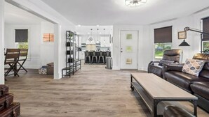 Ein modernes Wohnzimmer mit einer Ledersofa, einem Holztisch und einem Essbereich mit Stühlen, sowie eine Küche im Hintergrund.