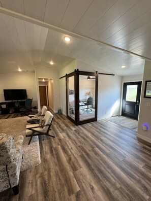 Un amplio salón con un televisor grande, asientos cómodos y piso de madera.
