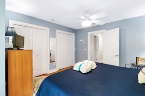 Ein Schlafzimmer mit einem Bett, einem Deckenventilator und einem Schreibtisch mit einem Computer.