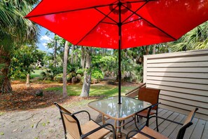 An outdoor patio with a table and chairs, a red umbrella, and a wooden fence. - 3 Story Condo - Bonus Room Upstairs! (Hilton Head Island)