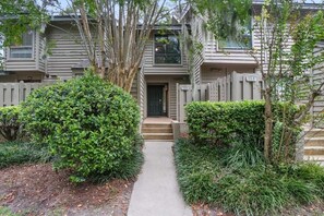 A two-story residential building with a front entrance, a small porch, and a pathway leading to the door.