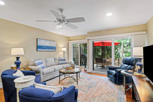 A living room with a sofa, armchairs, a coffee table, a TV, and a ceiling fan.