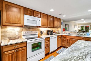 A modern kitchen with wooden cabinets, a white microwave, a stove, and a dishwasher. - 3 Story Condo - Bonus Room Upstairs! (Hilton Head Island)