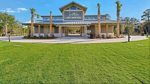 A modern two-story house with a large front porch, surrounded by a well-maintained lawn and palm trees. - 3 Story Condo - Bonus Room Upstairs! (Hilton Head Island)