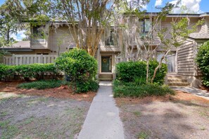 A two-story house with a front porch, a pathway leading to the door, and a small front yard with trimmed bushes.