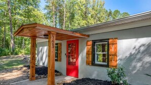 Una cabaña rústica con porche de madera, puerta roja y ventana con contraventanas.