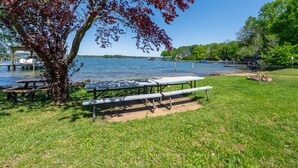 A lakeside picnic area with benches and a table, surrounded by trees and a clear view of the lake.